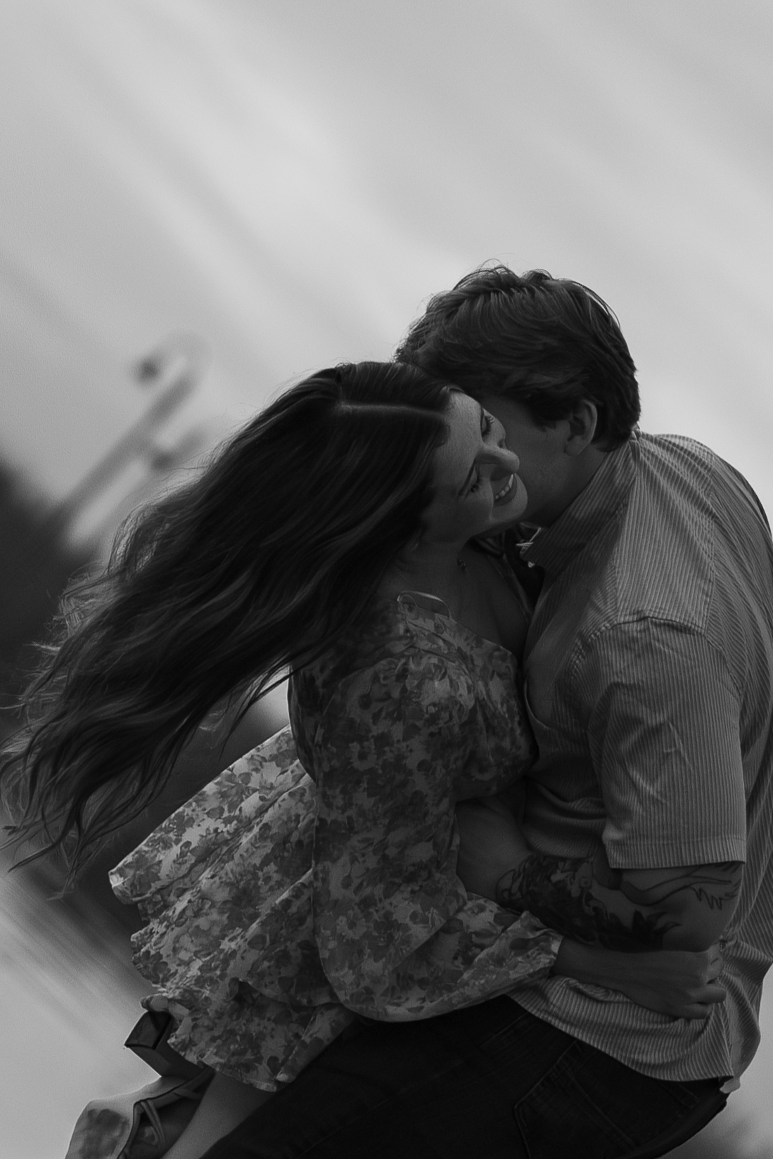 Black and white photo of a couple kissing, her hair blowing in the wind, from a couples session.