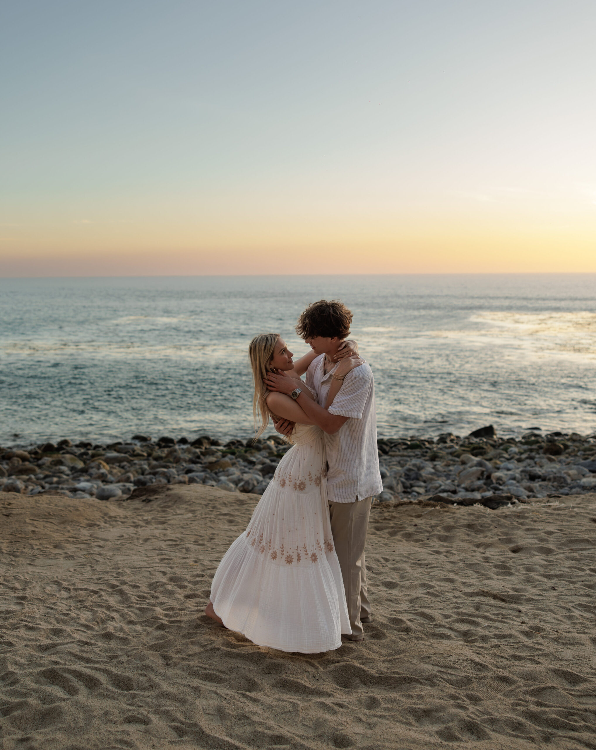 A couple embracing on a rocky beach at sunset, from a couples session by CBK Studios.