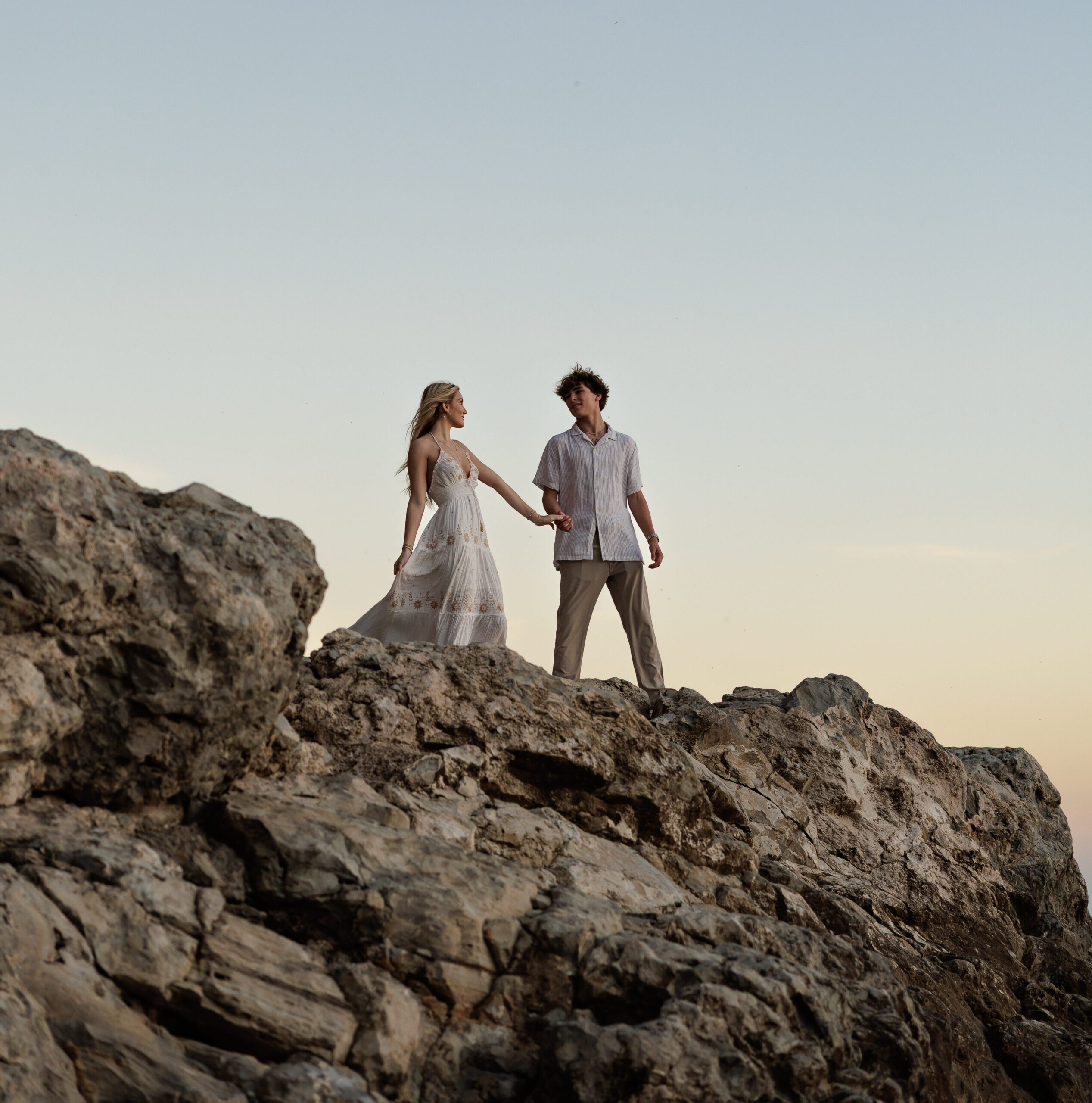 A couple holding hands on a rocky outcrop above the sea as the light fades, from a couples session.