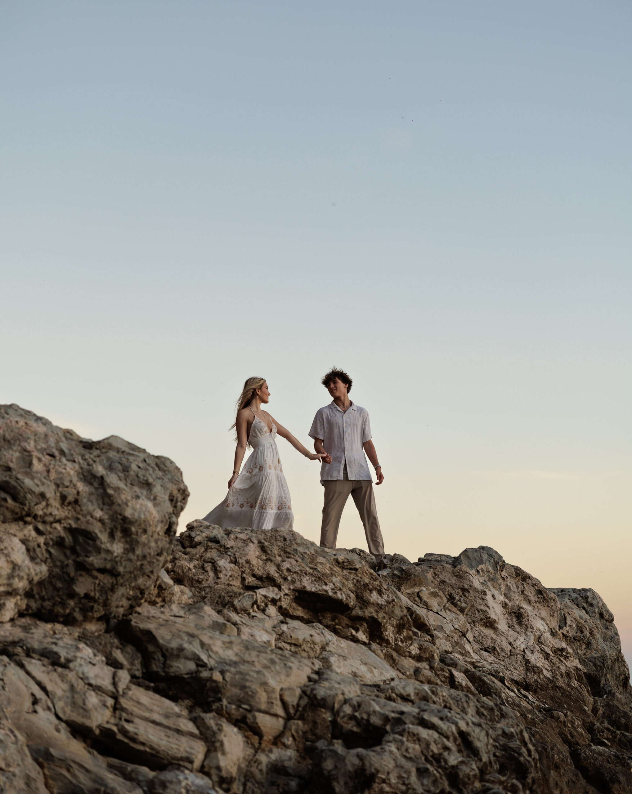 A couple holding hands on a rocky outcrop above the sea at dusk, from a couples session.