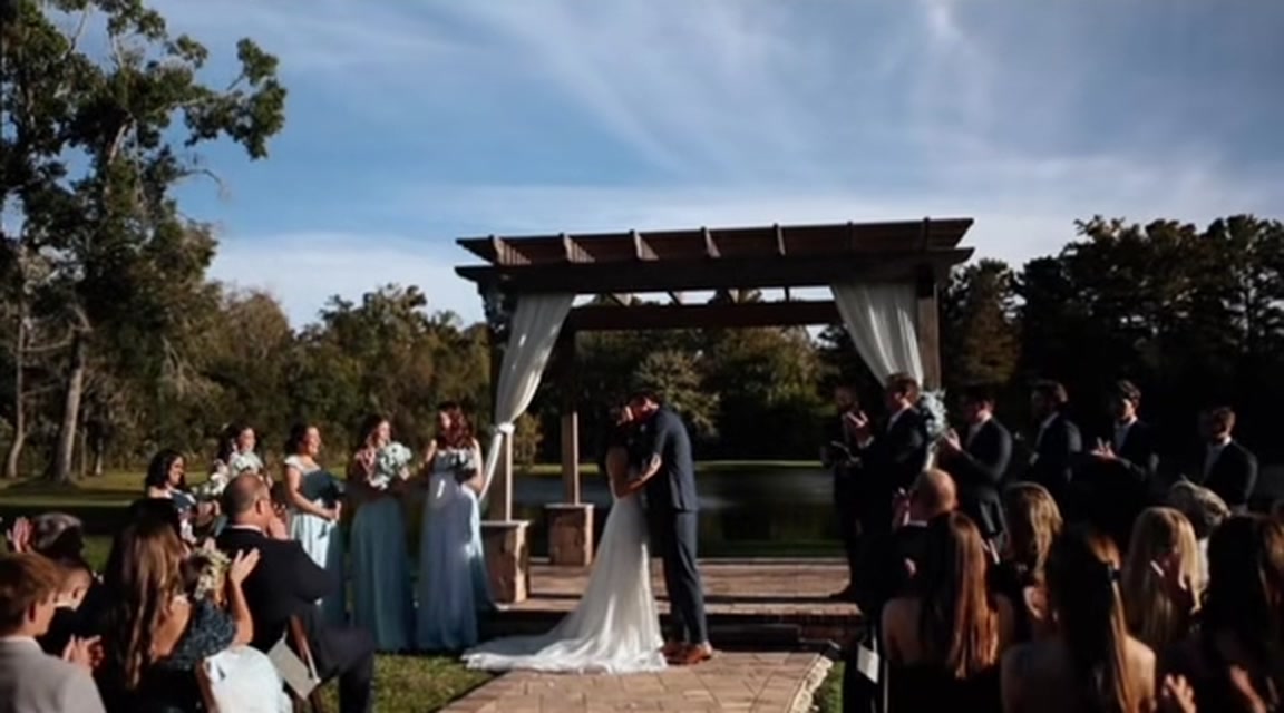 First kiss under a draped pergola beside a lake at a CBK Studios wedding, from the wedding film