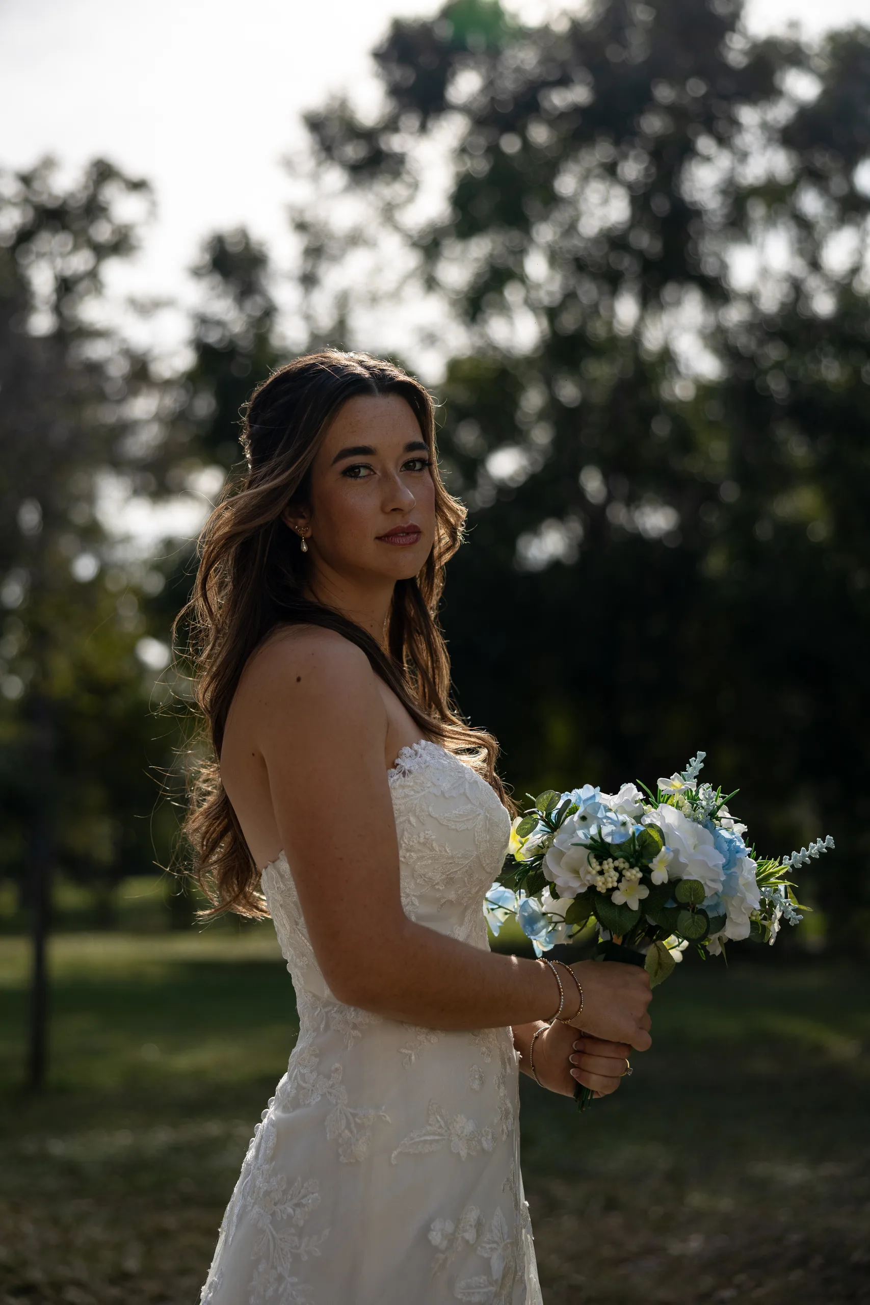 Bride with a blue and white bouquet under the trees at Cypress Creek Farmhouse, Orlando FL