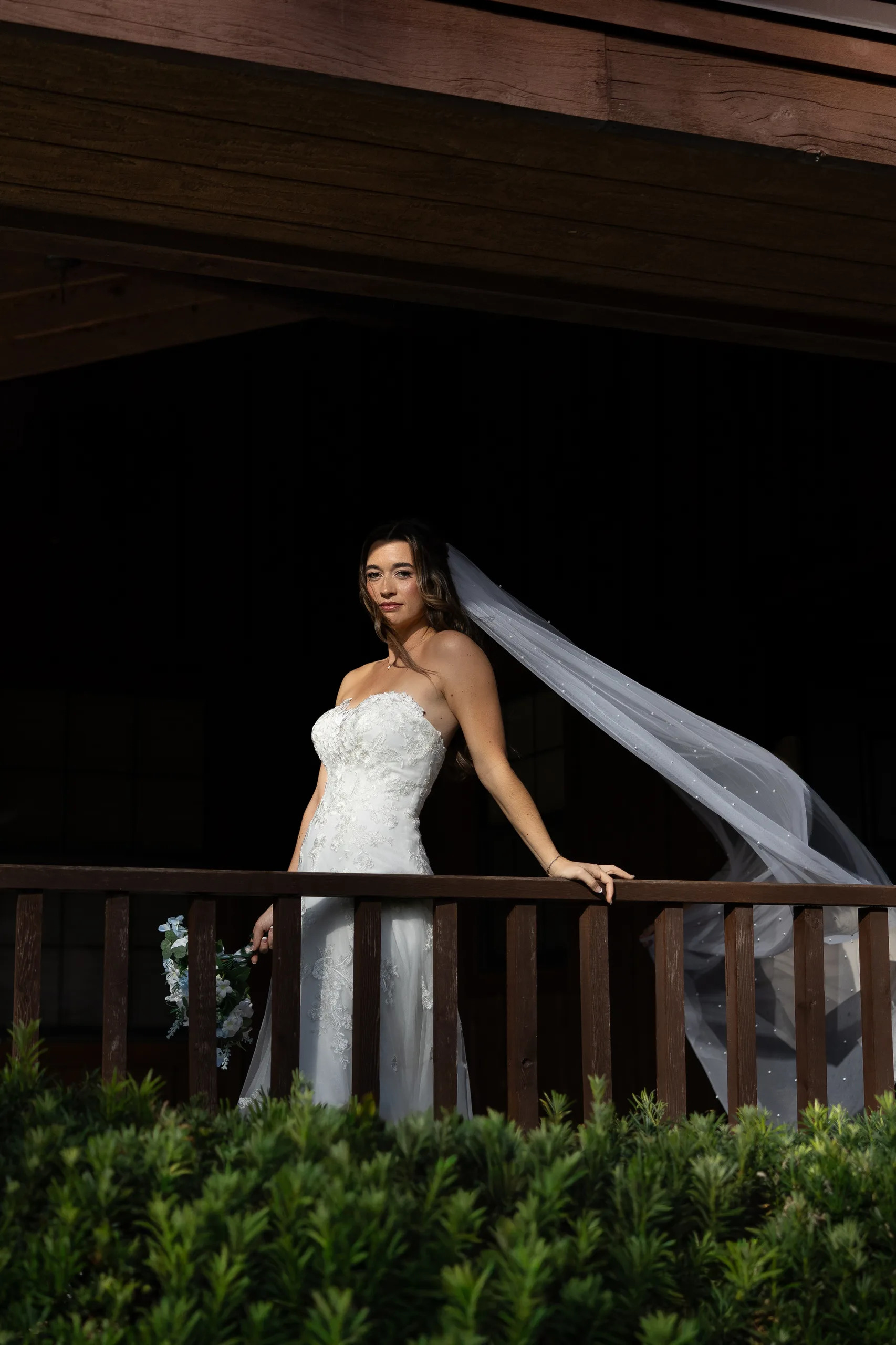 Bride on the porch railing with her veil in the wind at Cypress Creek Farmhouse, Orlando FL