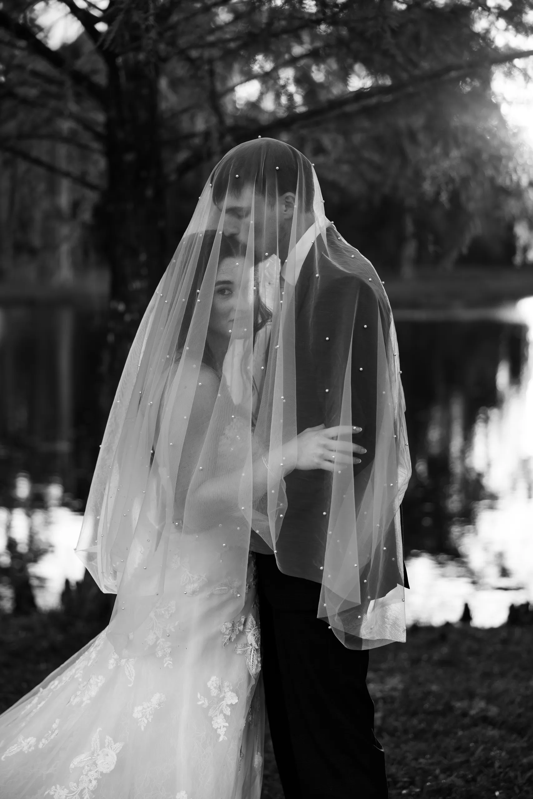 Bride and groom embracing under the veil by the pond at Cypress Creek Farmhouse, Orlando FL