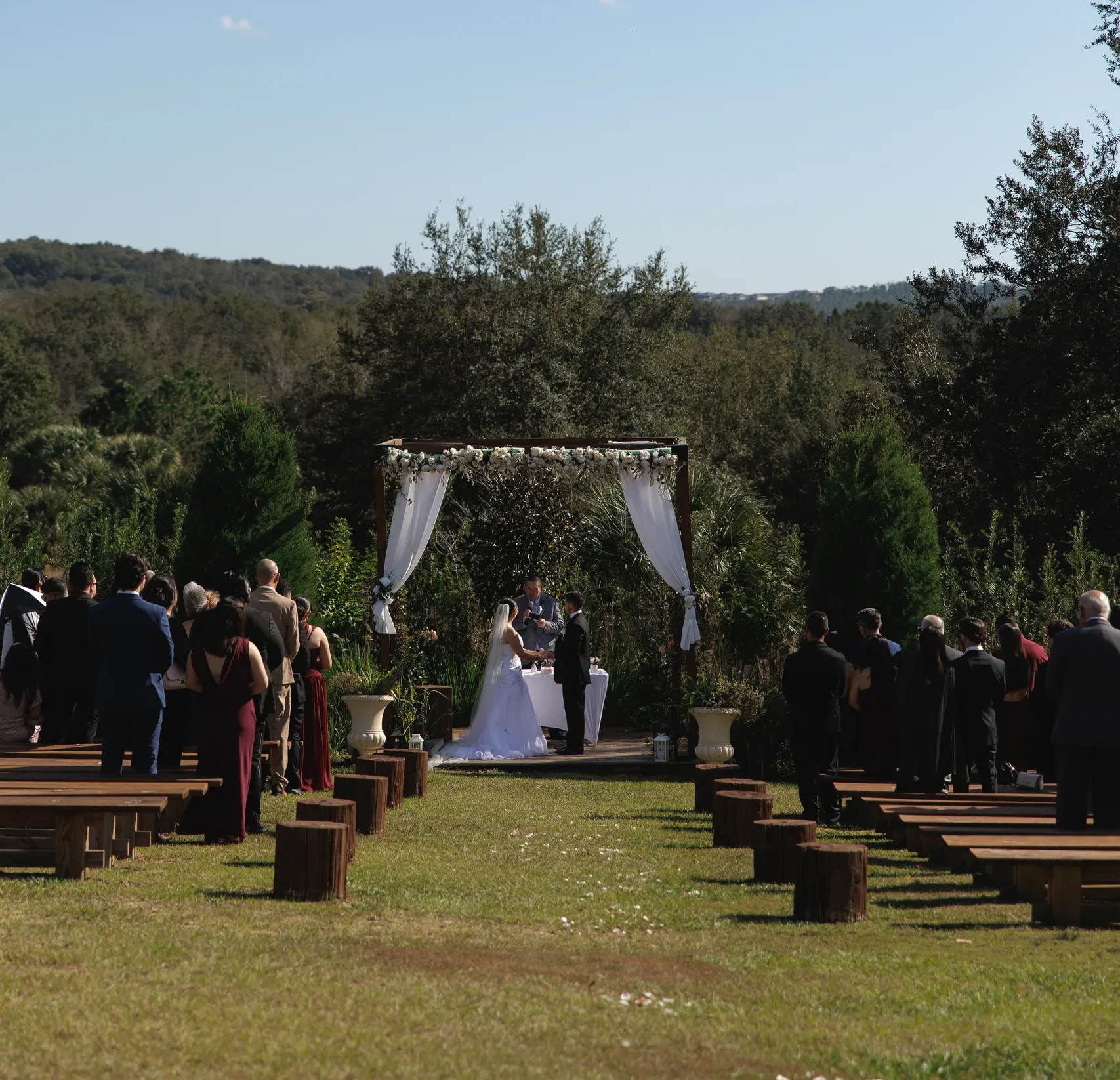 Hillside outdoor ceremony with wooden bench seating and rolling tree-lined views at The Hill House, Clermont FL