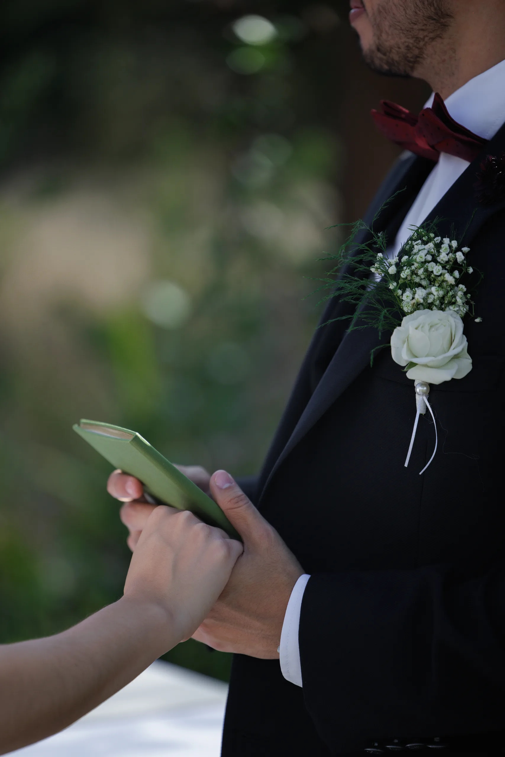 Groom holding a green vow book, white rose boutonniere pinned to his tux, at The Hill House, Clermont FL