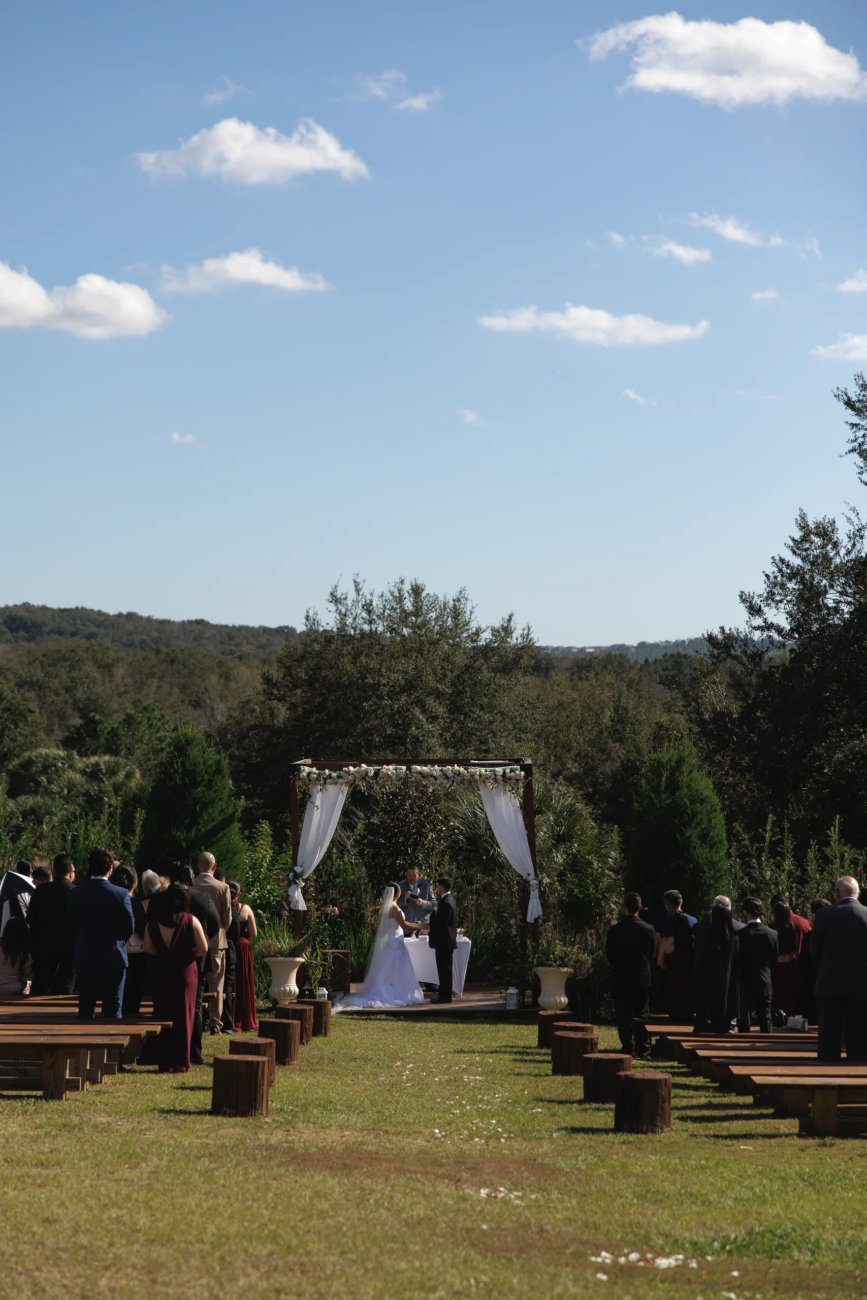 Hillside outdoor ceremony with wooden bench seating and rolling tree-lined views at The Hill House, Clermont FL