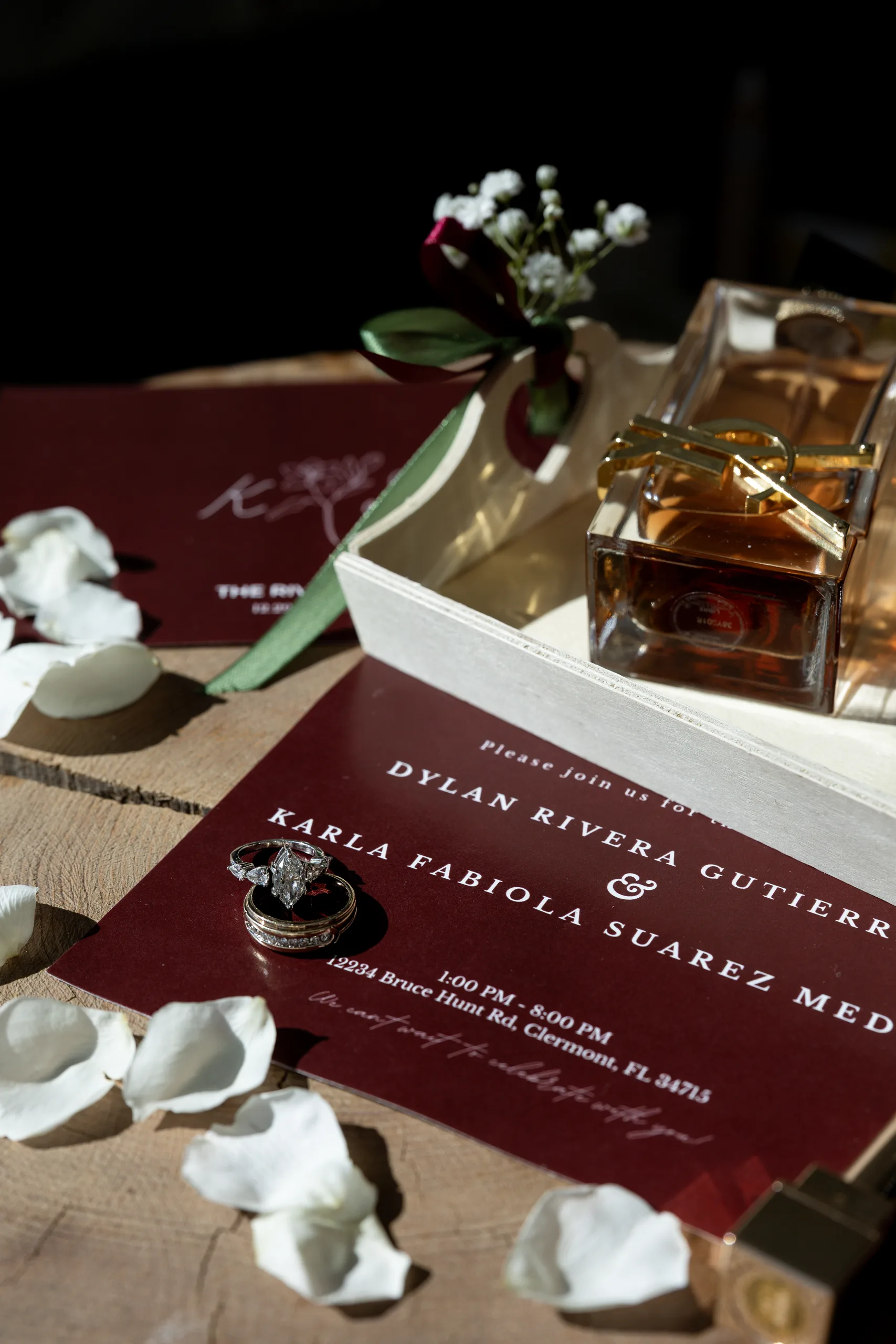 Burgundy invitation suite, wedding rings, and perfume styled on wood at The Hill House, Clermont FL