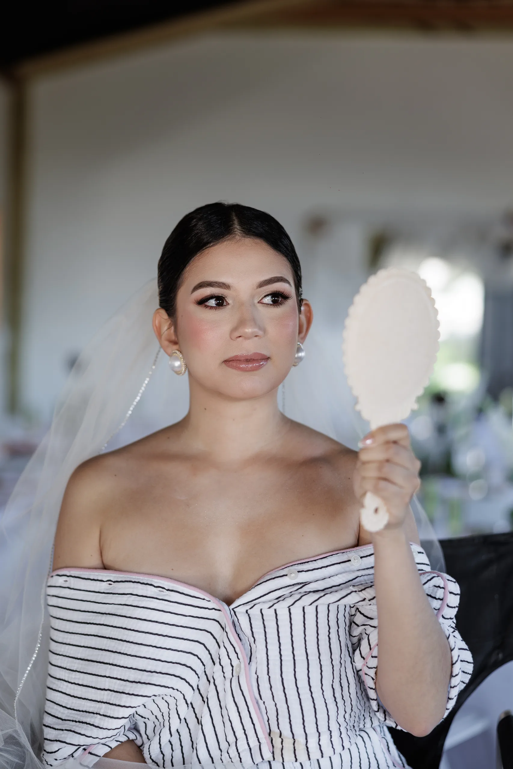 Bride in a striped robe checking her makeup in a hand mirror while getting ready at The Hill House, Clermont FL