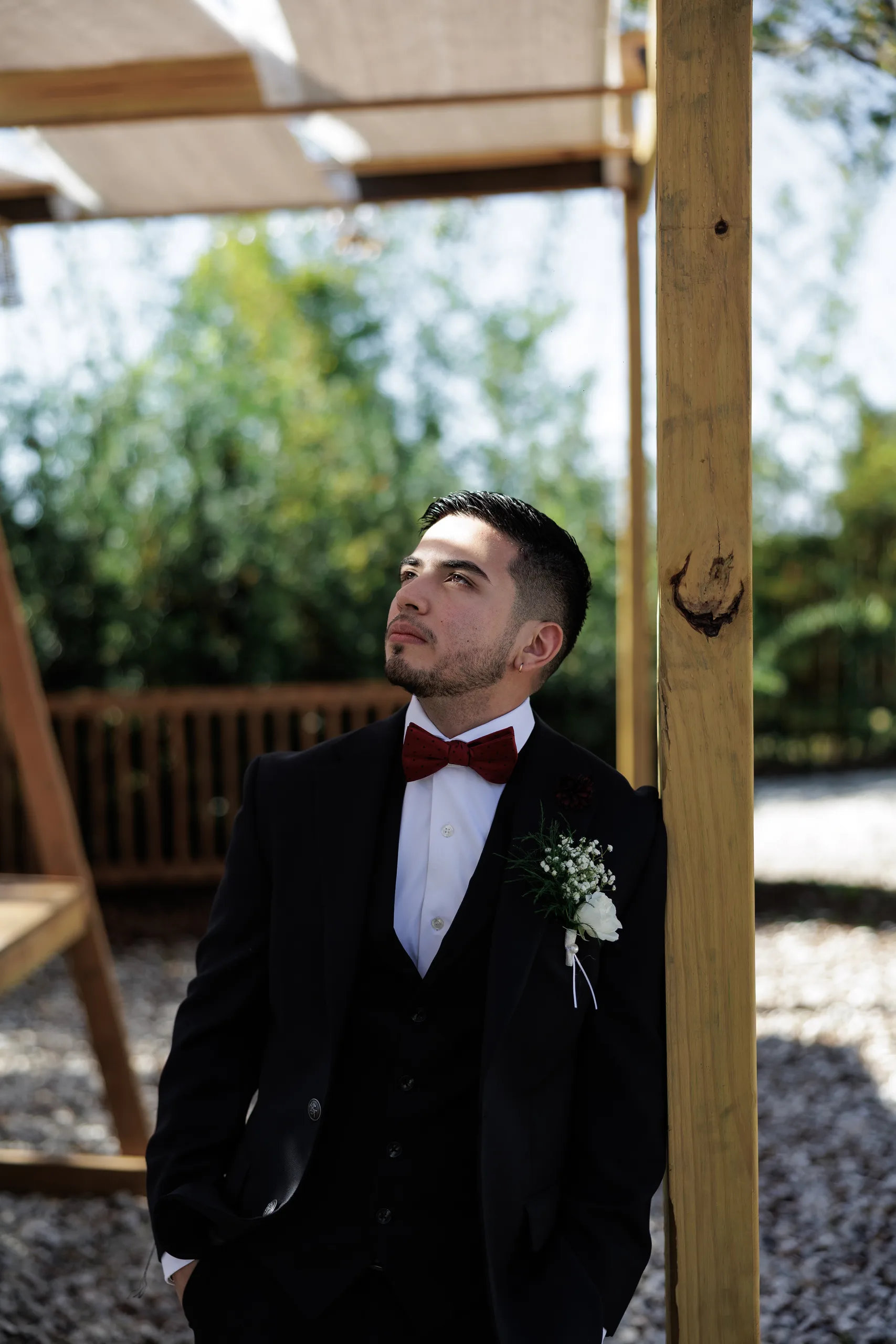 Groom in a burgundy bow tie leaning on a timber pergola post at The Hill House, Clermont FL