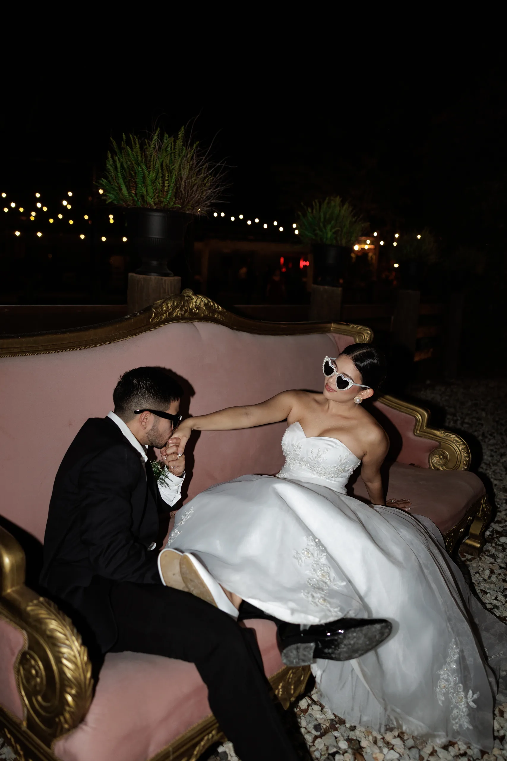 Groom kissing the bride's hand on the pink vintage sofa under string lights at The Hill House, Clermont FL