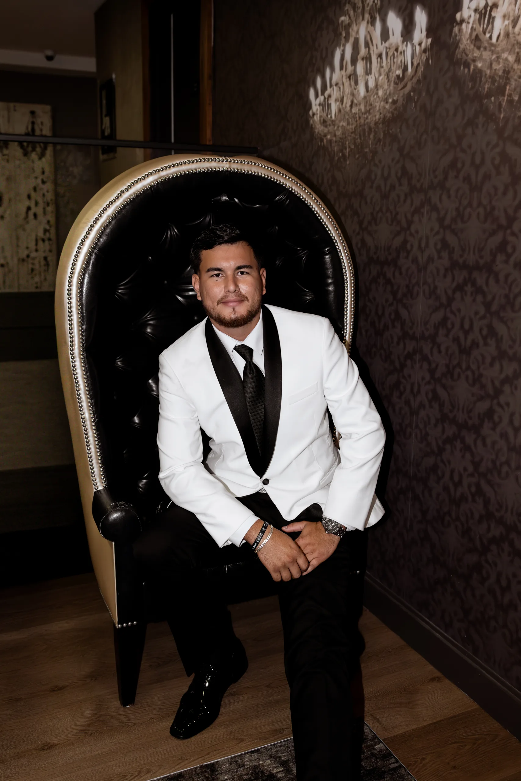 Groom portrait in the tufted black armchair against damask wallpaper at The J House Greenwich, Greenwich CT