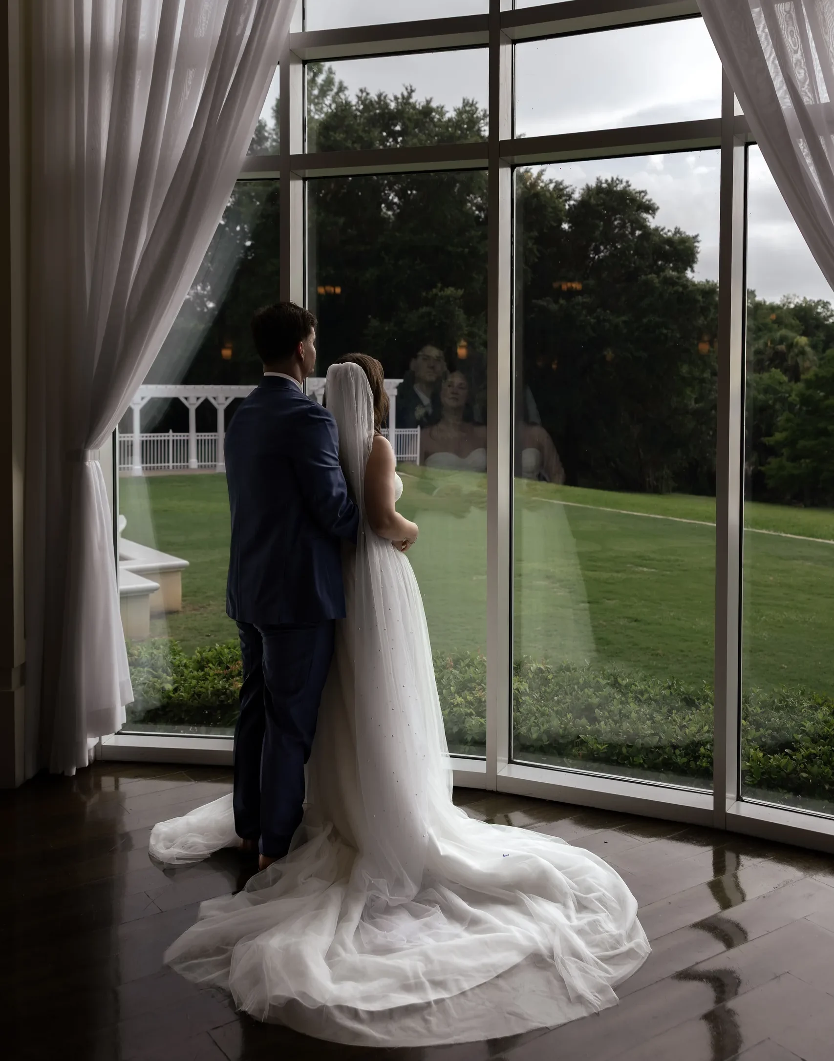 Bride and groom looking out over the grounds through the windows at Lake Mary Events Center