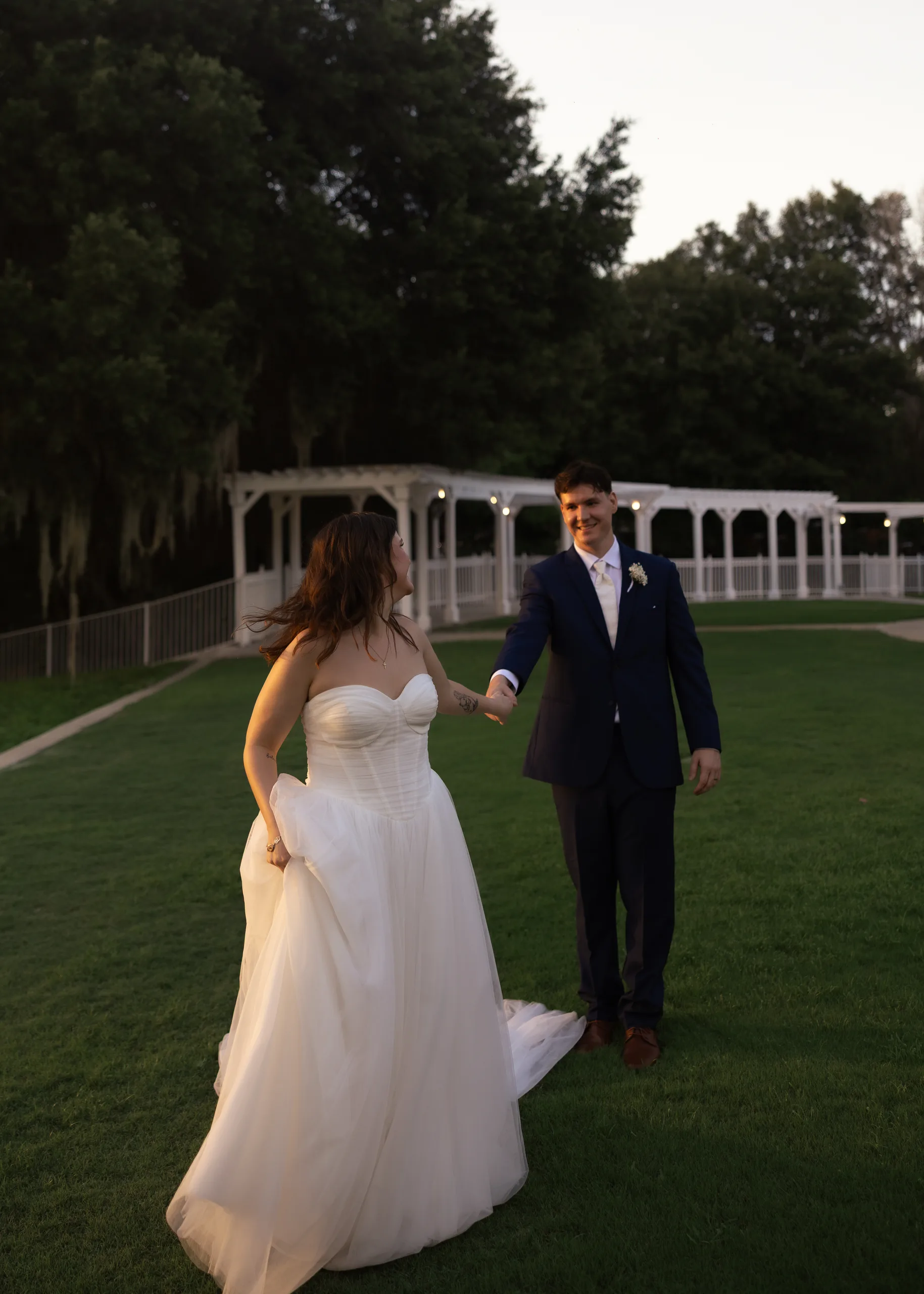 Bride and groom walking hand in hand across the lawn at dusk at Lake Mary Events Center