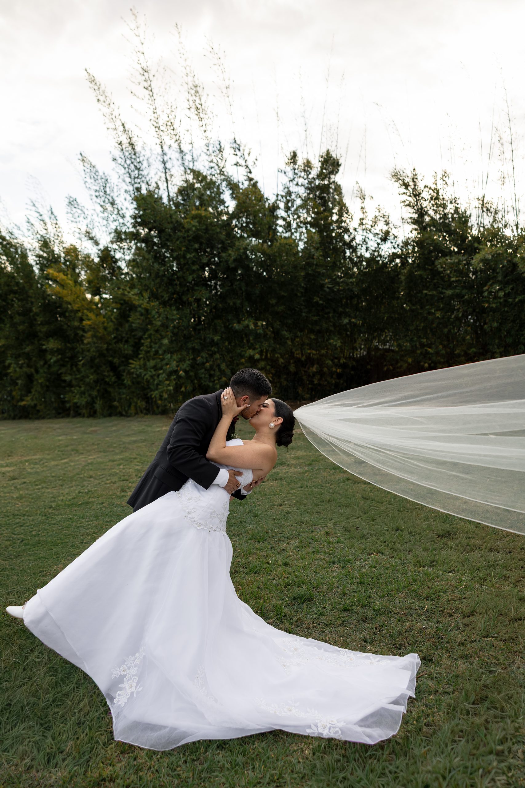 A groom dipping his bride for a kiss on the lawn at The Hill House, Clermont, FL, her veil trailing across the grass.